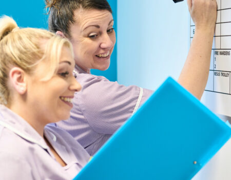 Two healthcare support workers writing on the patient board with patient notes
