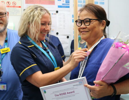 Helen pinning a rose badge onto Alis lanyard