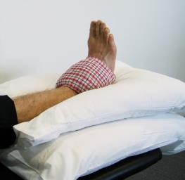 An ankle being rested on two pillows and supported with an ice pack