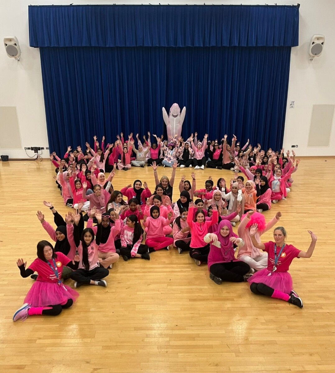 Challney High School for Girls students and stuff sitting in the shape of a breast cancer ribbon