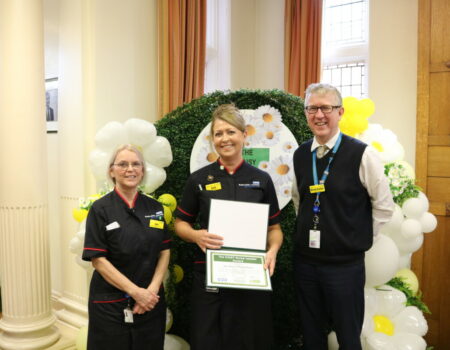 Bill and David with Liz, holding her DAISY Nurse Leader award